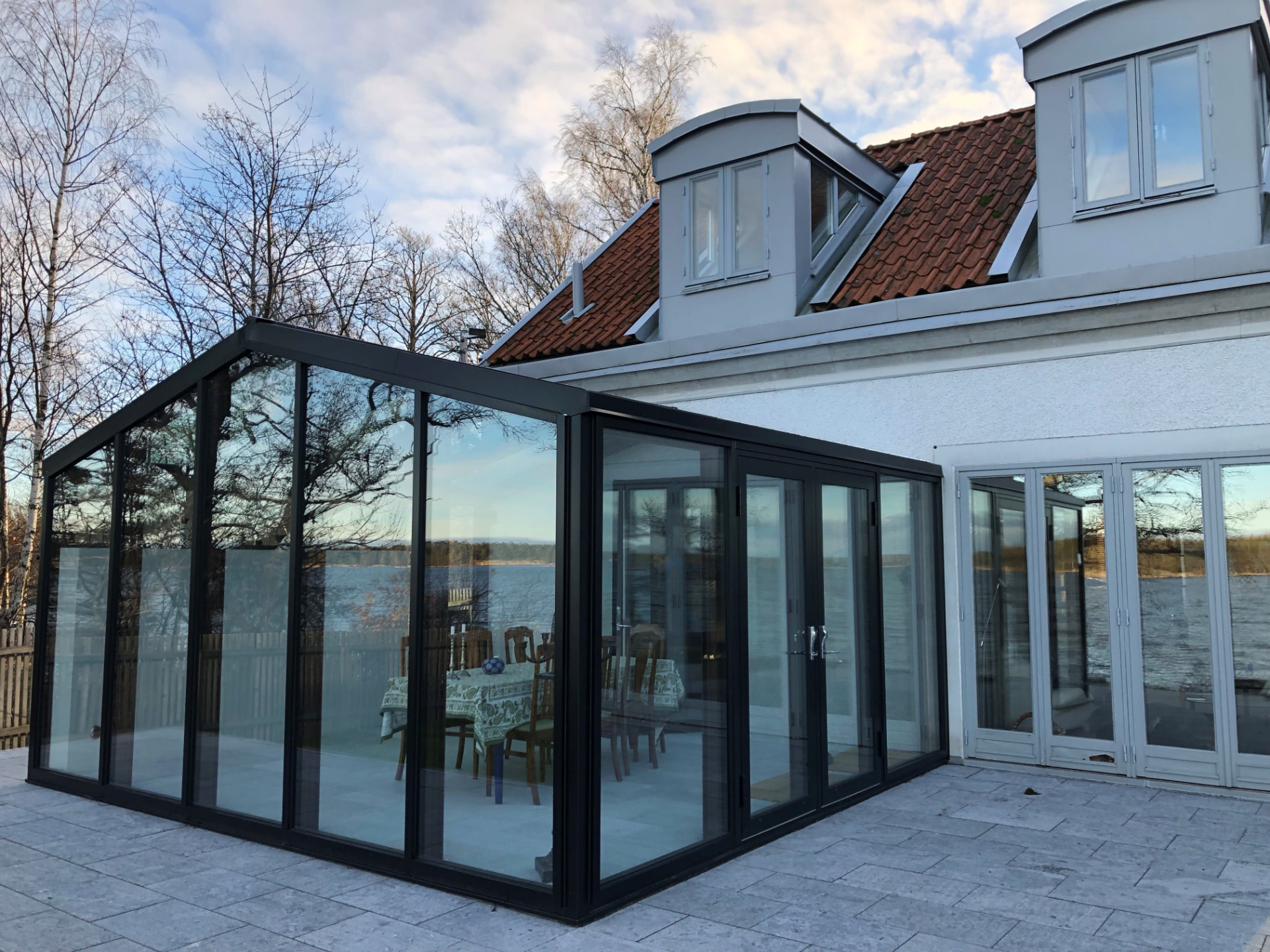 Uterum i aluminium med sadeltak mot huset, sett från hörnet med utsikt över sjön