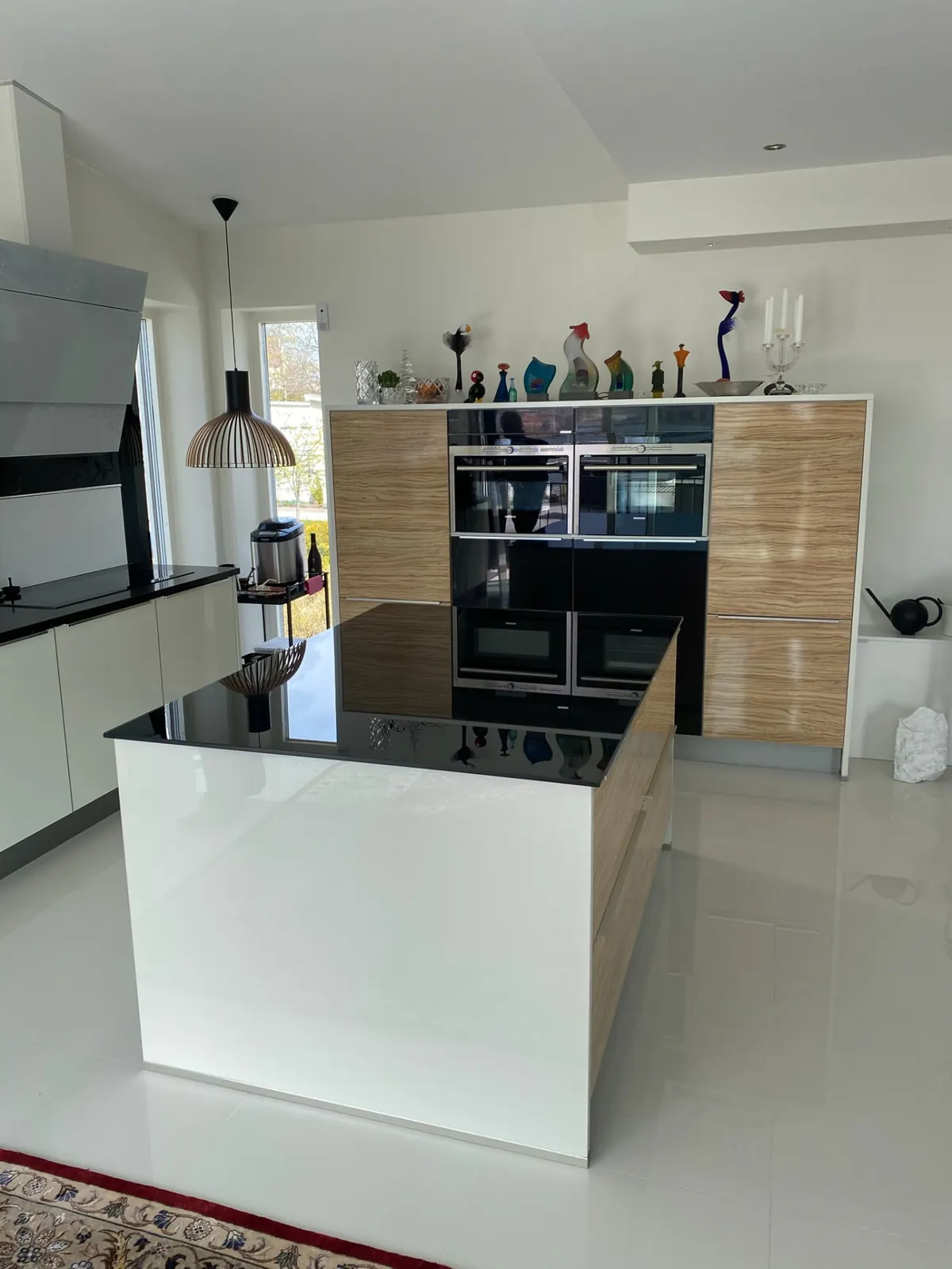 Kök med högblank svart bänkskiva och stänkskydd i glas, vita skåp och ljusa trädetaljer
