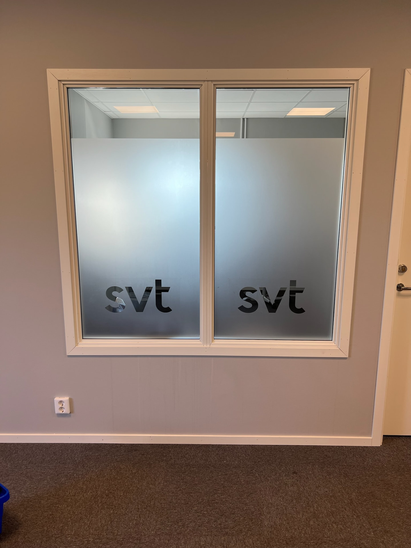 Innerfönster i en kontorsvägg med frostad film på rutorna, där en logotyp är konturskuren ur filmen så den syns klar genom glaset