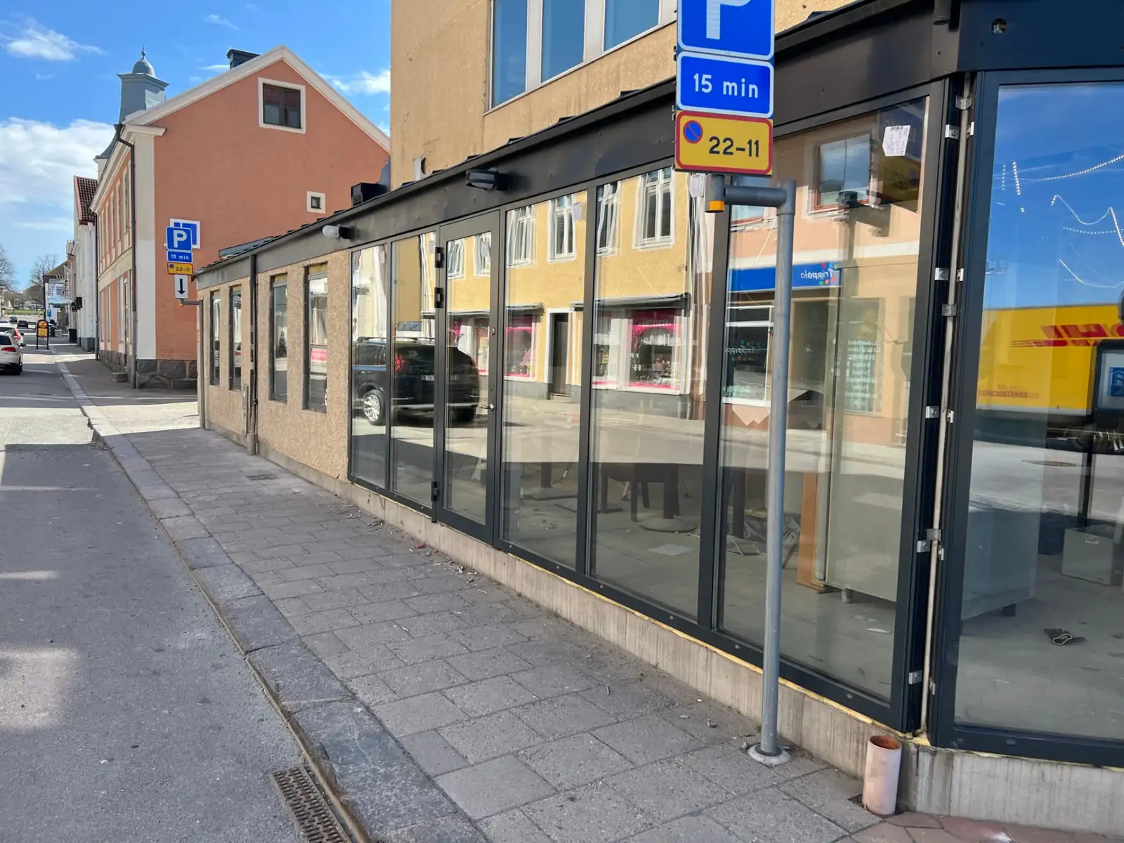 Butikslokal mot gatan med nya glaspartier och pardörr i svart aluminium, där gatan och husen speglas i glaset